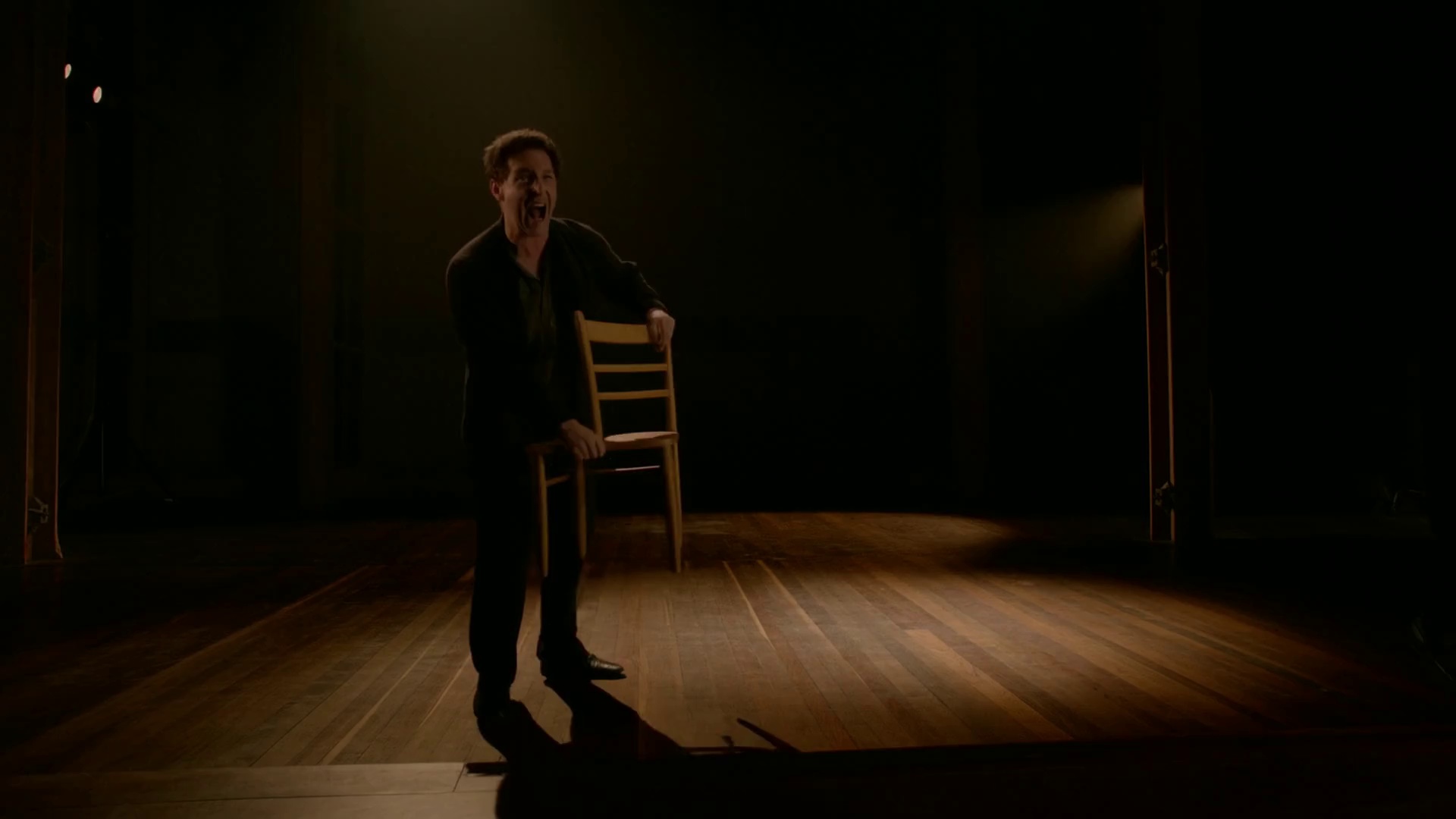 The actor in the image shouts passionately and throws a chair across the stage, dramatic lighting, camera pushes forward and tilts for intensity