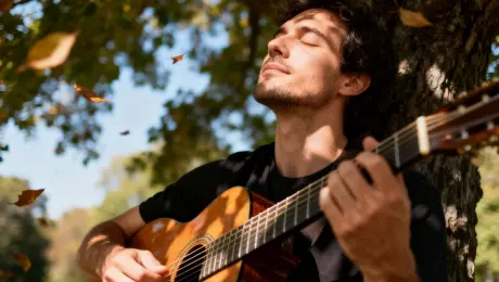 A man sits under a tree in a park, playing an acoustic guitar with his eyes closed, fully absorbed in the music. Dappled sunlight filters through the leaves, creating shifting patterns of light on him and his guitar. Cinematography: Starts with a close-up on his strumming hand, then slowly tilts up to his face to capture his soulful expression. The camera has a gentle sway, as if moving to the music's rhythm. Style & Atmosphere: Authentic, soulful, and intimate. The dappled light is dynamic, creating a warm and rhythmic mood. Environment & Details: The wood grain of the guitar and the vibration of the strings are visible. Leaves occasionally drift down in the background, which is soft and out of focus. Technical Specs: HD, 50mm prime lens effect, warm color grading, a visual representation of music.