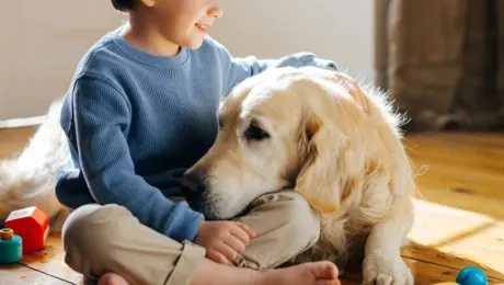A little boy sitting on the floor with his golden retriever, both looking at each other lovingly, soft natural light from a window, lifestyle photography, heartwarming and realistic