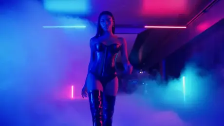 A confident dancer in leather corset and thigh-high boots walking through a foggy nightclub, bold strut, neon lights reflecting off her body, camera follows from low angle, cinematic energy