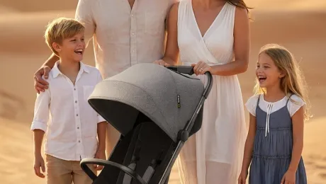 A commercial product photo in a desert setting, featuring a baby stroller as the main product and four human models: a father, a mother, a son, and a daughter. Professional posing, clean composition, bright lighting, realistic details, suitable for e-commerce catalog display.