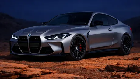 BMW M4 (2024 model) in a cinematic outdoor scene, featuring clean silver-gray metallic paint with sharp, controlled reflections. Lit only by soft ambient light-no direct sunlight or harshhighlights. The ground is covered in rugged warm orange rock textures, with layered formations in the foreground enhancing depth. The sky is a deep, saturated blue with
no clouds or glare, reflecting subtly on the car. Lighting is moody andstudio-like, with no long shadows, delivering strong color contrast and high-end automotive ad quality with precise composition and spatial depth. --raw