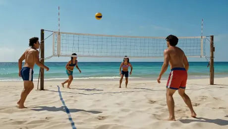 A cinematic wide shot of a sun-drenched beach in the Maldives. A group of energetic young people playing beach volleyball on pristine white sand. The ocean is crystal clear, shimmering in shades of turquoise and azure, with gentle ripples reflecting the bright sunlight. In the background, iconic overwater bungalows and lush palm trees are visible. Action-packed movement with sand splashing as a player jumps for a spike. 8k resolution, photorealistic, shot on 35mm lens, high dynamic range, vibrant colors, fluid motion, masterpiece.