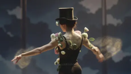 A character adorned with blooming flowers and wearing a black top hat dances gracefully across the frame, with the camera gliding smoothly to follow every movement. A soft, warm golden glow emanates from the character’s figure, drifting gently in sync with the dance—blending seamlessly with light and shadow to weave a dreamlike, mysterious atmosphere brimming with poetic charm and visual dynamism.