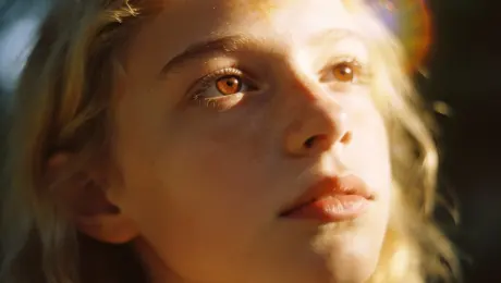 Analog-style portrait of a mystical blonde girl with sun-kissed skin and soft brown eyes. Shot on Cinestill 400D film aesthetic, subtle halation, gentle grain, and warm cinematic tones. Low-angle composition with natural light, creating an artistic, nostalgic, and slightly melancholic mood. Feels intimate, dreamy, and timeless.