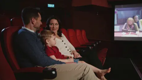 Change the scene to a movie theater, where three people are sitting in theater seats watching a movie. Pay attention to the lighting and shadow effects.