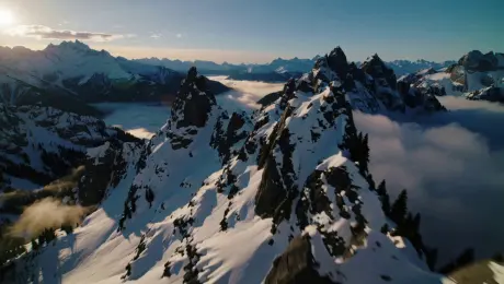 Cinematic drone shot, flying rapidly over jagged snow-capped mountain peaks, golden hour sunset lighting hitting the ridges, clouds misting around the mountains, photorealistic, 8k resolution, highly detailed, dramatic shadows.