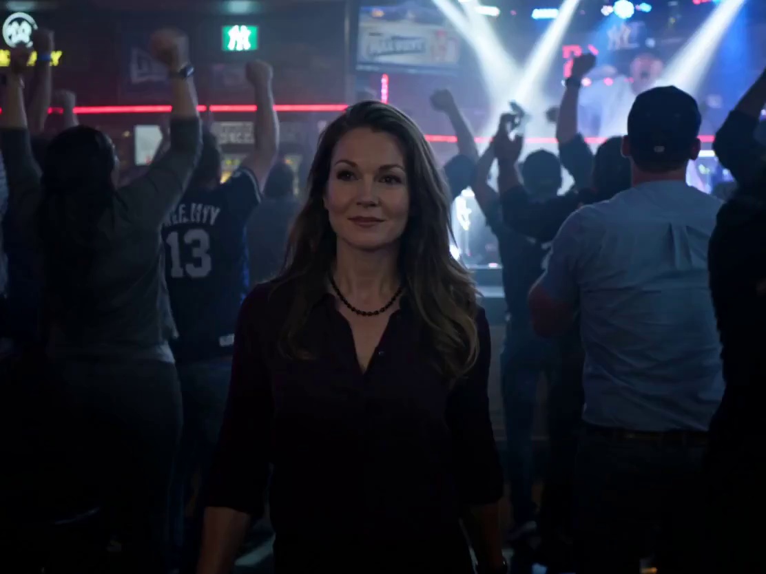 Use @ Reference Image as the main character, keeping facial features and body proportions consistent throughout. She is a 30-year-old women. Cinematic time-freeze short film, 15 seconds, ultra-realistic, shot on Arri Alexa Mini, 35mm lens, moody sports bar interior lighting with neon accents, volumetric haze, dynamic hard shadows, shallow depth of field.

[0:00–0:03] A packed, dimly lit sports bar, time flowing normally. Steadicam frontal medium shot tracking her walking confidently through absolute chaos. On the blurred TVs in the background, the Yankees have just clinched the World Series. The crowd is erupting in pure euphoria. As he walks, he raises his right hand and snaps.

[0:03–0:06] At the snap, a subtle spherical shockwave bursts from her fingertips with air distortion and light refraction, expanding outward. Everything freezes mid-explosion. Thick arcs of golden beer suspend in the air, with individual glistening droplets visible. Popcorn kernels float motionless. People are frozen mid-cheer and mid-air in leaping embraces. Volumetric neon light catches the suspended dust and liquid. Absolute silence.

[0:06–0:09] Only she moves. her footsteps echo slightly. The camera moves backward as he walks through the frozen celebration, observing calmly. she casually ducks under an arc of frozen, splashing beer. she notices a cluster of floating popcorn, reaches out, and plucks a single kernel from the air.

[0:09–0:11] sHe stops in front of a frozen women wearing a Yankees jersey, her face locked in an ecstatic, tearful scream, arms raised for a high-five. The main character tilts her head, gently adjusts the brim of the frozen women's Yankees cap, nods slightly, and softly says: “perfect.”

[0:11–0:15] She turns, tosses the popcorn kernel into her mouth, and crunches it. She faces the camera, smirks, and snaps again. A stronger reverse shockwave restores motion. The beer completes its splash, the cheering roar instantly returns, and fans land their jumps. She walks away as the camera pushes through the wildly celebrating crowd. Fade to black.

Sound: deafening bar roar/celebration → snap → deep shockwave/bass drop → absolute silence → footsteps → sharp popcorn crunch → “perfect” → snap → reverse shockwave → deafening celebration returns.