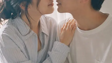 9:16 vertical — Japanese Fuji film style couple portrait, two subjects  Fujifilm analog aesthetic (Pro 400H / Superia feel), soft pastel tones, slight green-magenta shift, low contrast, gentle highlight roll-off, fine film grain, subtle halation  bright natural daylight, diffused sunlight through window, soft shadows, airy atmosphere  young Japanese couple, natural minimal makeup, realistic skin texture, slight imperfections  female outfit: oversized button-up shirt with loose shorts, relaxed fit, soft casual styling   male outfit: simple t-shirt or light shirt, clean and understated  hair: natural, slightly tousled for both  pose: close intimate distance — sitting or standing close together; the girl gently leaning toward him, one hand lightly resting on his shoulder or chest; the boy slightly leaning in, faces close, almost touching, capturing the moment just before a kiss  expression: soft smiles or gentle gaze toward each other, relaxed and natural, emotional connection visible  camera: close framing (waist-up), eye-level, intimate distance, slight handheld feel  setting: minimal indoor near window, light curtains, clean soft background  lighting: diffused daylight, gentle highlight bloom, soft shadow transitions  mood: warm, romantic, intimate everyday moment, natural affection  quality: ultra-realistic, analog film look, fine grain, slight softness, natural imperfections