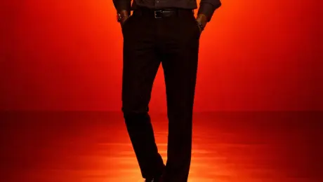 Generate a cinematic minimal portrait of a solitary man standing in an intense orange to red gradient environment, strong silhouette lighting, deep shadow contrast, reflective glossy floor, symmetrical composition, minimal