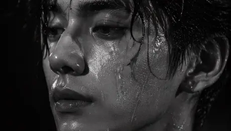 生成一张高度逼真、高对比度的黑白肖像，强调湿润的皮肤质感和戏剧性的光影效果。
A striking black and white close-up portrait of a {argument name="subject description" default="handsome young Asian man"} with {argument name="hair style" default="messy wet hair sticking to his forehead"}. His face and neck are glistening, covered in highly detailed {argument name="skin texture detail" default="water droplets and sweat"}. He has an intense, melancholic gaze directed off-camera to the left. The lighting is dramatic and high-contrast, emphasizing his sharp jawline, full lips, and specular highlights on the wet skin against a {argument name="background" default="pitch-black background"}. Shot in a photorealistic, high-fashion editorial style with cinematic chiaroscuro.