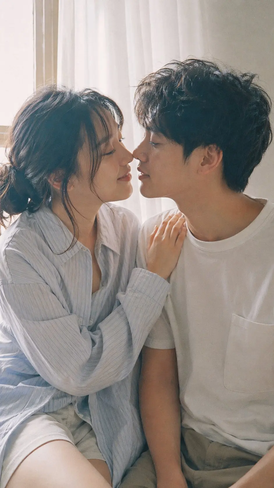 9:16 vertical — Japanese Fuji film style couple portrait, two subjects Fujifilm analog aesthetic (Pro 400H / Superia feel), soft pastel tones, slight green-magenta shift, low contrast, gentle highlight roll-off, fine film grain, subtle halation bright natural daylight, diffused sunlight through window, soft shadows, airy atmosphere young Japanese couple, natural minimal makeup, realistic skin texture, slight imperfections female outfit: oversized button-up shirt with loose shorts, relaxed fit, soft casual styling male outfit: simple t-shirt or light shirt, clean and understated hair: natural, slightly tousled for both pose: close intimate distance — sitting or standing close together; the girl gently leaning toward him, one hand lightly resting on his shoulder or chest; the boy slightly leaning in, faces close, almost touching, capturing the moment just before a kiss expression: soft smiles or gentle gaze toward each other, relaxed and natural, emotional connection visible camera: close framing (waist-up), eye-level, intimate distance, slight handheld feel setting: minimal indoor near window, light curtains, clean soft background lighting: diffused daylight, gentle highlight bloom, soft shadow transitions mood: warm, romantic, intimate everyday moment, natural affection quality: ultra-realistic, analog film look, fine grain, slight softness, natural imperfections