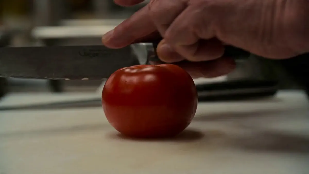 A master chef, 60s, with a white cane hooked on the counter edge, works alone in a chaotic Michelin-star kitchen during dinner rush.
Shot 1: Extreme close-up — his fingertips ghost across the surface of a tomato with surgical precision, mapping its shape before the knife descends in a blur.
Shot 2: Wide shot — the kitchen erupts around him, flames leaping, pans clanging, young chefs sprinting — but he stands absolutely still at his station, an eye of calm in the storm.
Shot 3: Over-the-shoulder shot — his hands move at impossible speed across the cutting board, paper-thin slices falling in perfect sequence without a single wasted motion.
Shot 4: Close-up on his face — nostrils flaring, head tilted slightly, reading the kitchen entirely through smell and sound, a faint smile crossing his lips.
Shot 5: He plates the dish by touch alone, sets it on the pass, and steps back — a young chef stares at the perfect dish in disbelief, then looks at him with wide eyes.
Raw and visceral, the film crackles with the tension of mastery existing beyond the limits of sight.