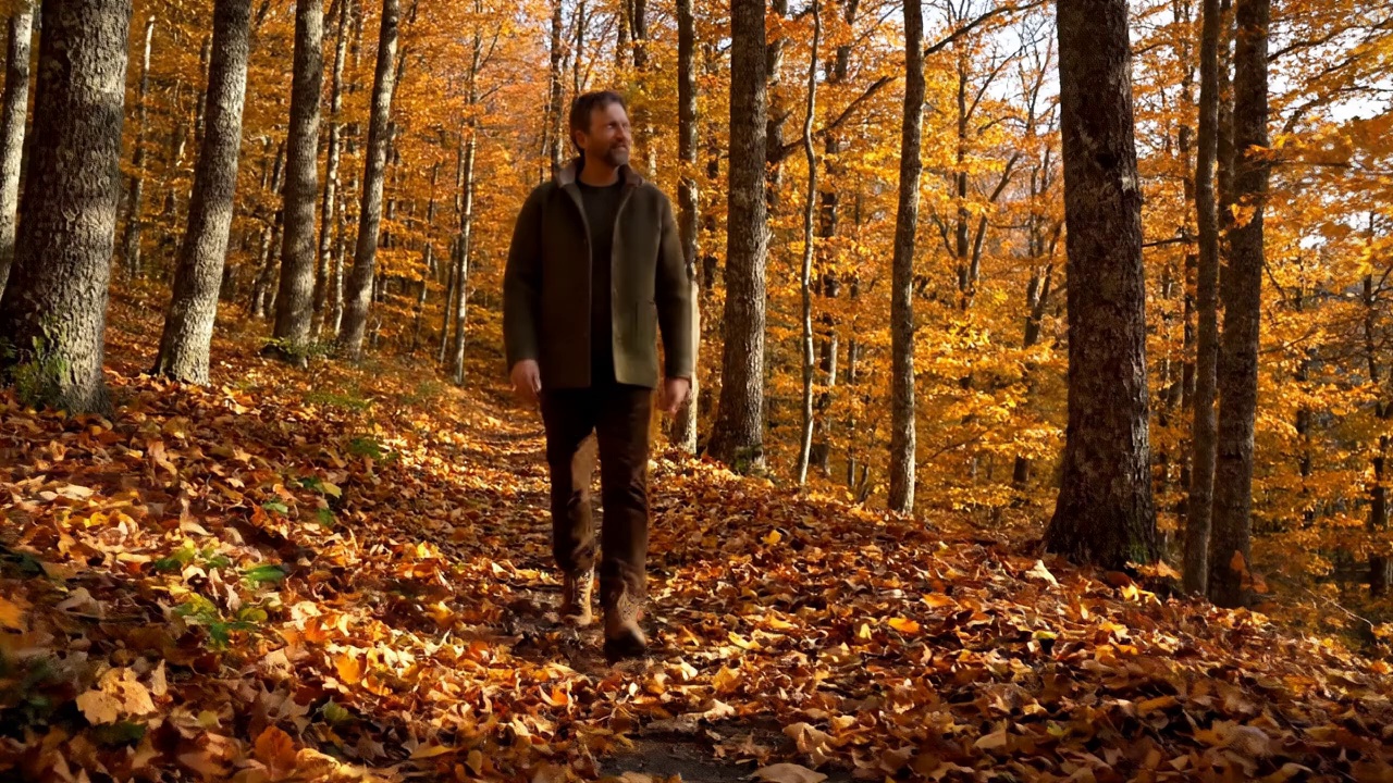 A man walking alone on a forest trail in autumn, leaves crunching underfoot. Birds chirp in the distance. He murmurs: "Feels good to be away from everything for a while."