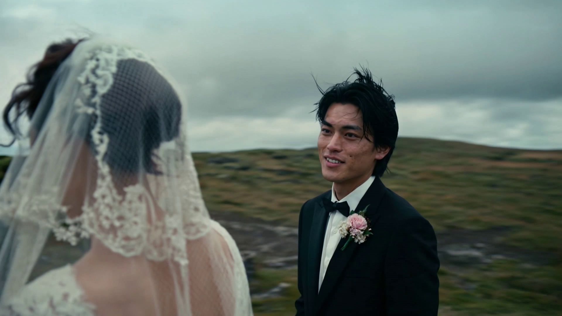 Long take. On a windy day in an Icelandic mountain range, @Male Protagonist says with a barely contained smile, "Do you think our wedding is too simple—like there's no one here to bless us?"

The camera circles the subjects to reveal @Female Protagonist standing opposite, smiling and replying, "The wind—the wind is their blessing to us."

Cinematic, handheld feel.